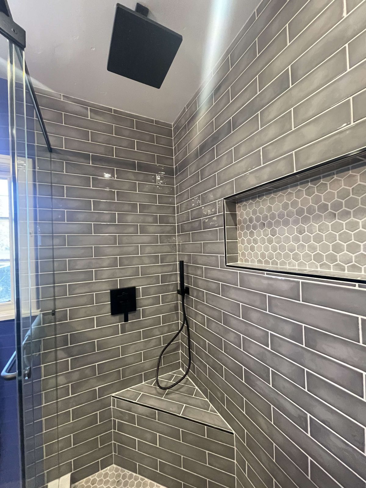 Finished walk-in shower with gray subway tile and hexagon niche